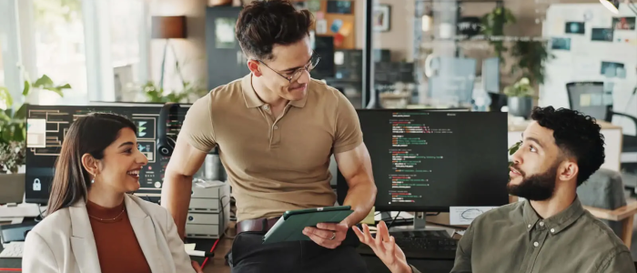 Three professionals chatting in front of computers.