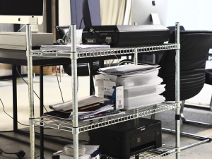 A wire stand with a printer sitting on one of the shelves